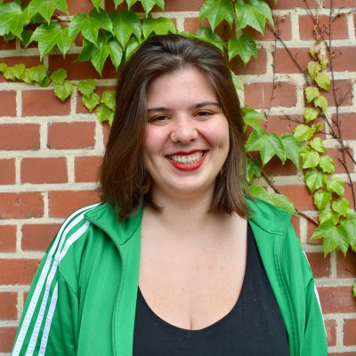 Das Bild zeigt die Geschäftsführung Lena. Sie steht vor einer mit Efeu bewachsenen Backsteinwand und lacht in die Kamera. © Servicestelle Jugendbeteiligung e.V., 2020 Das Bild zeigt die Geschäftsführung Lena. Sie steht vor einer mit Efeu bewachsenen Backsteinwand und lacht in die Kamera. © Servicestelle Jugendbeteiligung e.V., 2020