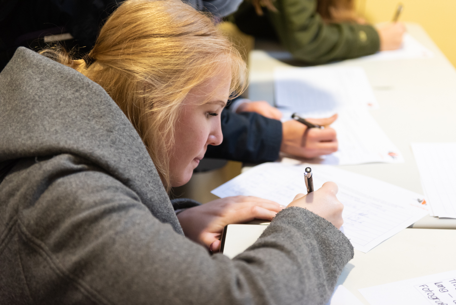 Einen junge Frau schreibt etwas auf ein Blatt. Sie hockt vor einem Tisch.