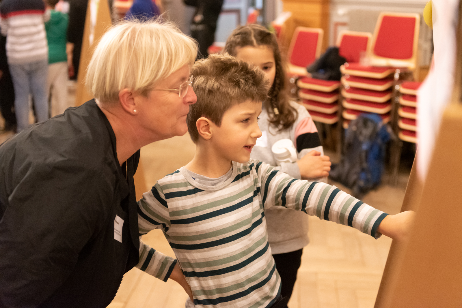 Zwei Kinder stehen mit ihrer Lehrerin vor einer Pinnwand und diskutieren über den Inhalt auf der Pinnwand. Ein Kind zeigt auf etwas. © Servicestelle Jugendbeteiligung e.V., 2020