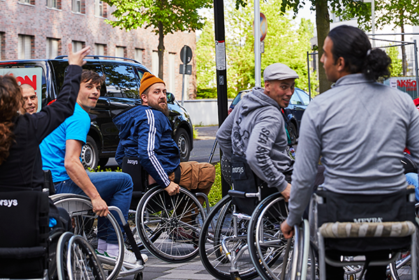 Das Bild zeigt sechs Menschen, die in Rollstühlen Basketball spielen. Eine Person versucht einen Basketball in den Korb zu werfen, die anderen Personen beobachten sie aufmerksam dabei. © Aktion Mensch e. V. / Servicestelle Jugendbeteiligung e. V./Anna Spindelndreier, 2019"