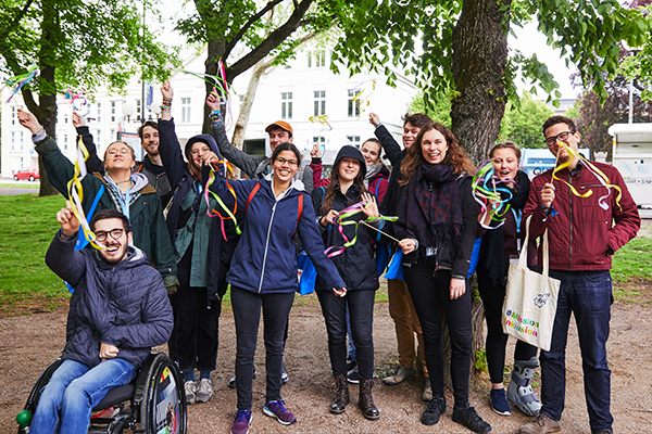 Das Bild zeigt eine Gruppe junger Menschen, die lachend posieren und Stäbe mit bunten Bändern schwenken © Aktion Mensch e. V. / Servicestelle Jugendbeteiligung e. V./Anna Spindelndreier, 2019"