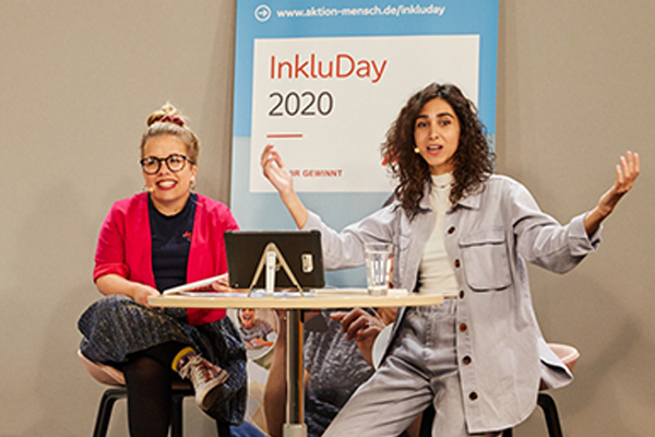 Auf dem Bild zu sehen sind Ninia und Suri, die beiden Moderatorinnen des InkluDay 2020. Sie sitzen an einem Tisch und lachen in die Kamera © Anna Spindelndreier, 2020