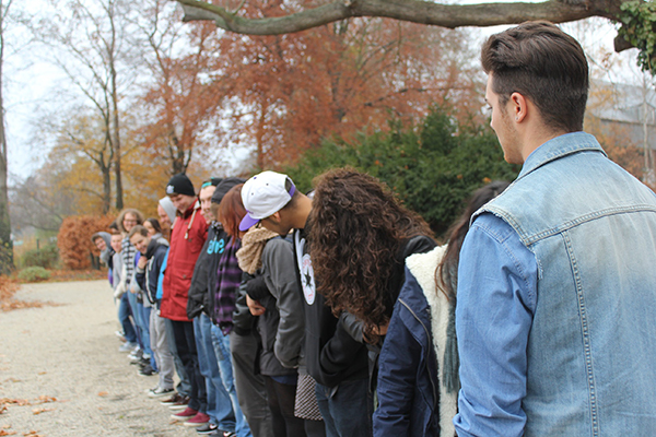 Das Bild zeigt eine Reihe von jungen Menschen, die auf einem Weg umgeben von herbstlichen Bäumen in einer Reihe stehen und sich zueinander umsehen. © Servicestelle Jugendbeteiligung e. V., 2018