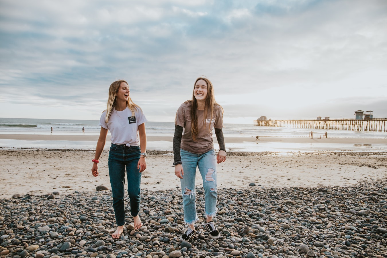 Auf dem Bild sind zwei Jugendliche lachend an einem Strand zu sehen.