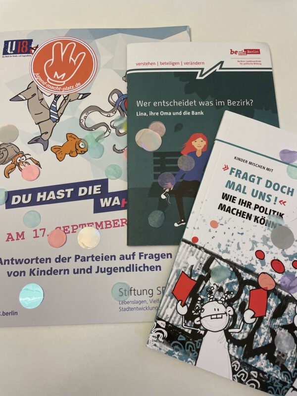 Auf einem Tisch liegen Infobroschüren zur Wahl und zu Beteiligungsmöglichkeiten, dazu Sticker und Konfetti © SJB, 2021