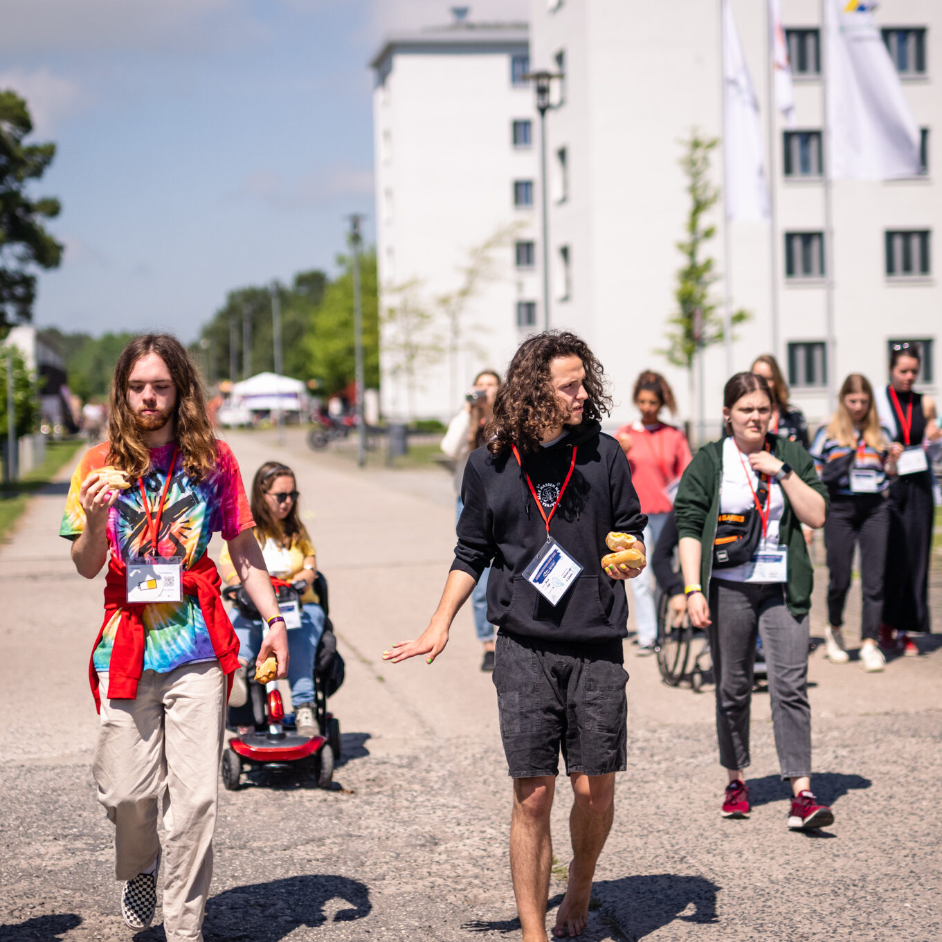 B: Eine Gruppe junger Menschen bewegen sich zu Fuß und im Rollstuhl, vor der Jugendherberge. Sie machen eine Führung mit.