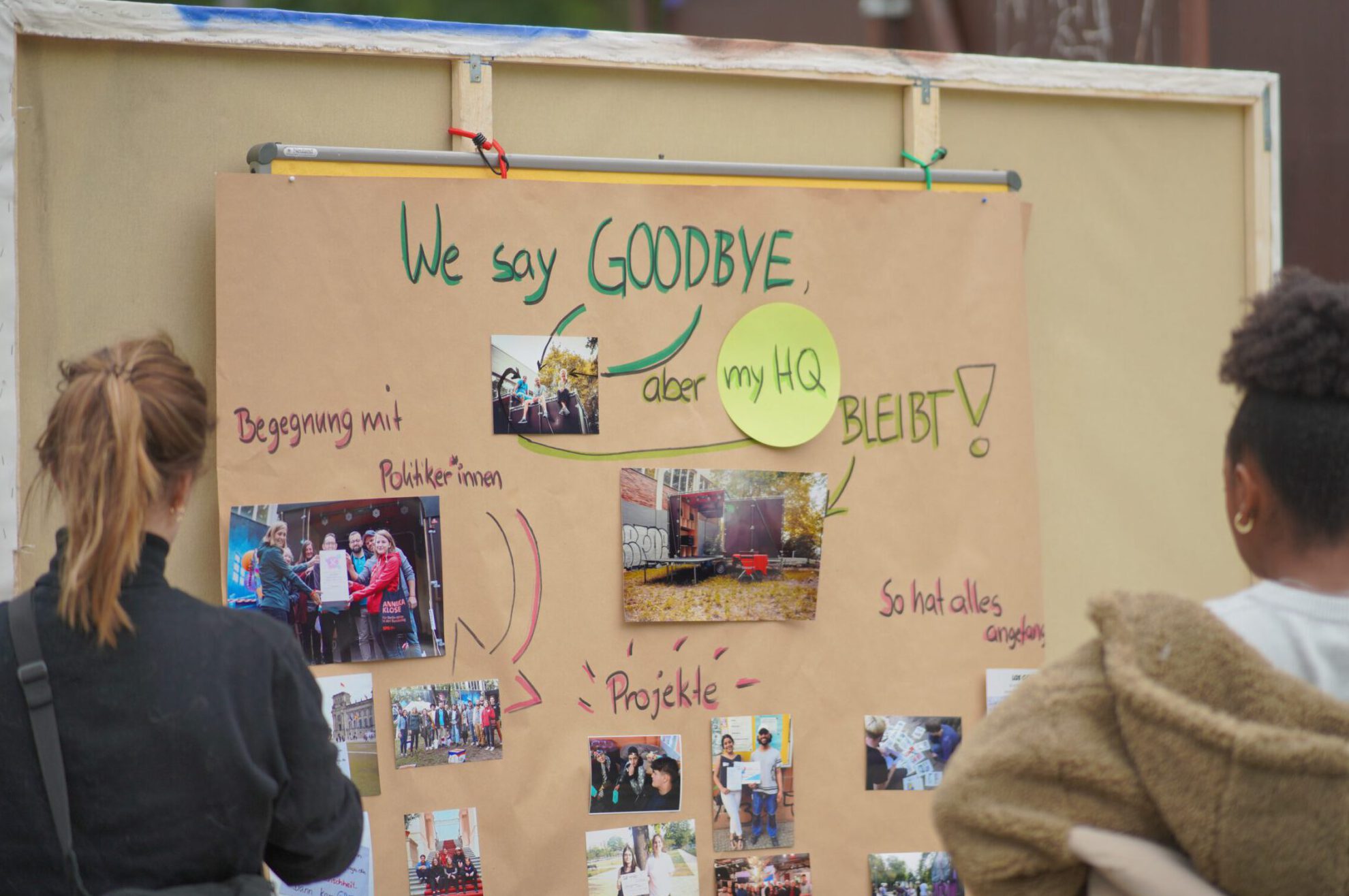 B:Auf dem Bild sieht man Menschen, die ein bemaltes Plakat anschauen, das Eindrücke aus dem Projekt Jugend Macht Platz bietet. Es ist überschrieben mit den Worten "We say goodbye. Aber das myHQ bleibt!"