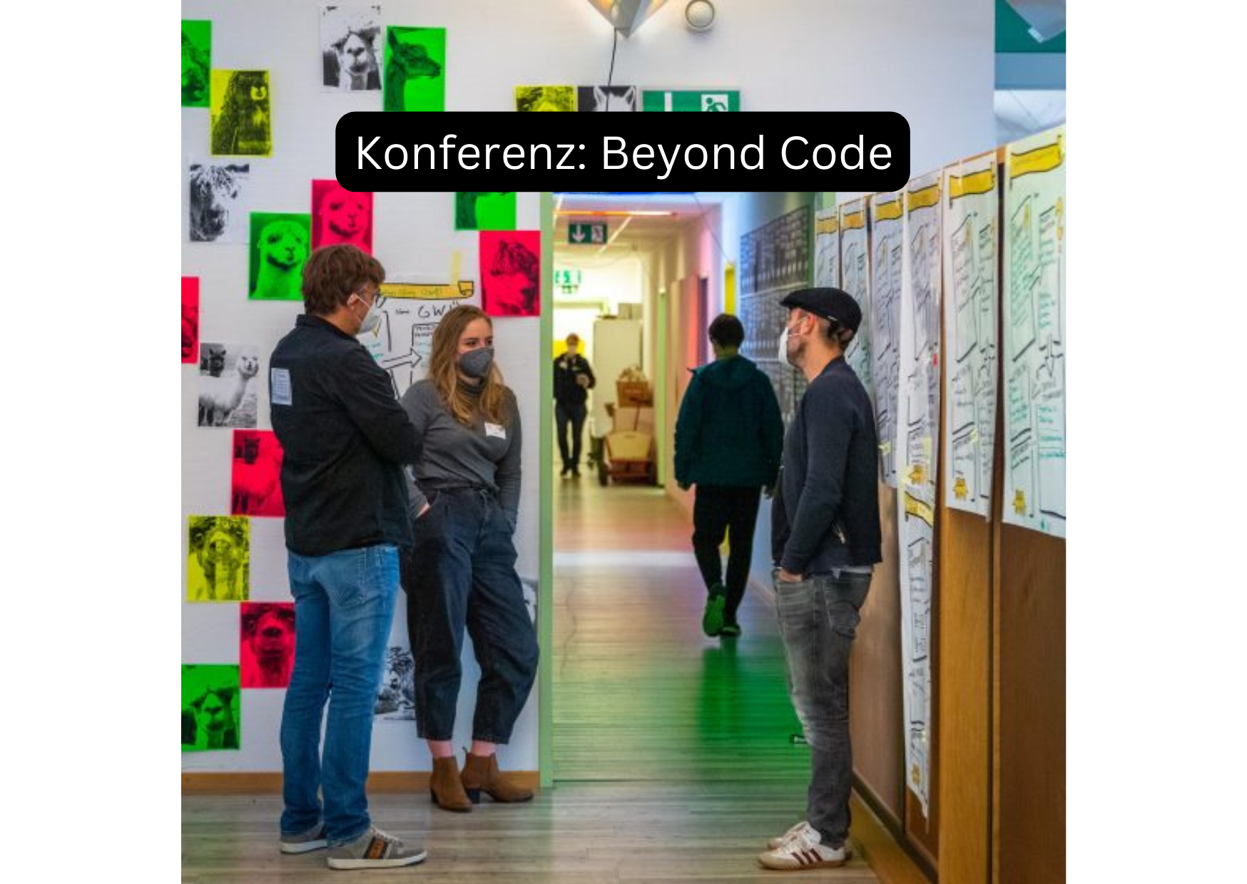 Drei junge Menschen tragen eine Maske, stehen in einem Flur und unterhalten sich. Der Flur ist mit Postern und Ähnlichem dekoriert. In weißer Schrift auf schwarzem Hintergrund steht die Überschrift "Konferenz: Beyond Code".