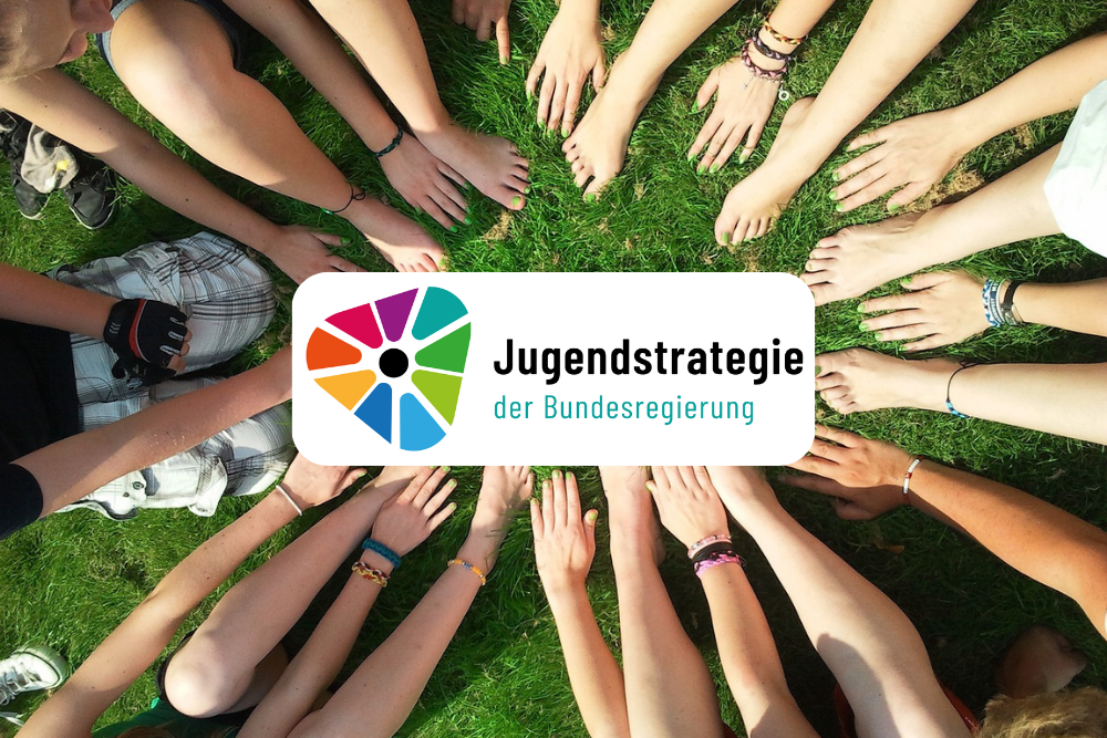 Es sind viele Arme junger Menschen abgebildet, welche sich alle mit den Händen in einer Mitte treffen. Im Vordergrund ist das Logo des Vereins ,,Jugendstrategie der Bundesregierung" abgebildet.