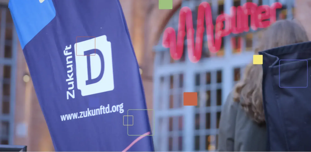 Bild von Zukunft d zeigt links eine Milane Fahne mit dem Zukunft D Logo und ihrer Webadresse (Zukunft.org) und rechts verschwommen ein Fenster mit rosa Lichtzug, sowie den Rucksack auf dem Rücken einer Person (von hinten)
